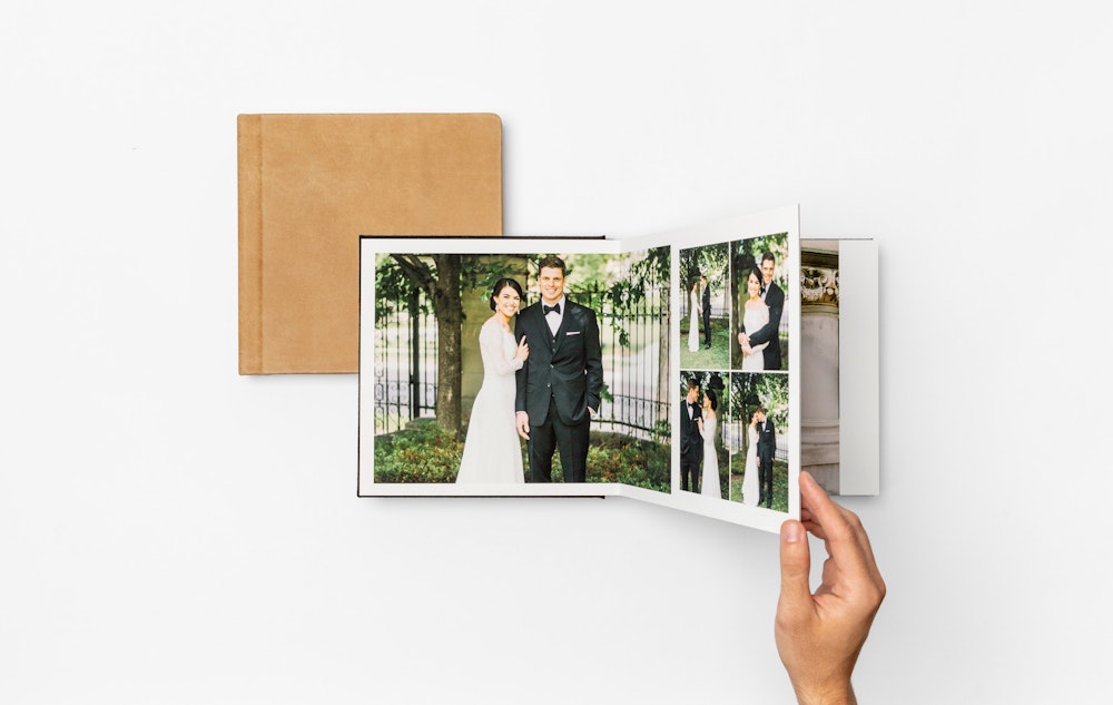 A hand turning the pages of a wedding album featuring photos, elegantly bound in a leather cover.