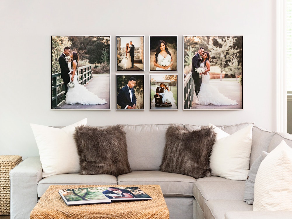 A living room with a gray sectional sofa, brown and white pillows, a wicker coffee table, and a wall display of six framed wedding prints above the sofa.